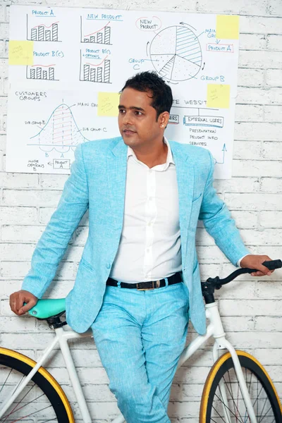 Startup project manager leaning on his bicycle in modern office