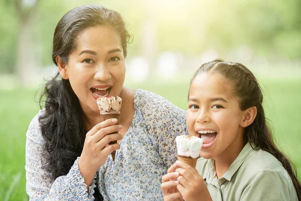 成年亚洲妇女和可爱的女孩咬冰淇淋和看着相机 而在一起在公园里度过 — 图库照片