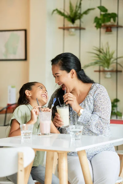 成年亚洲妇女和可爱的女孩笑着看着对方 同时喝着美味的奶昔在舒适的咖啡馆 — 图库照片
