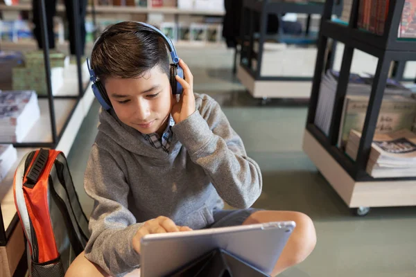 ヘッドフォンでポジティブな十代の少年は学校の図書館で Lection オンラインを見て — ストック写真