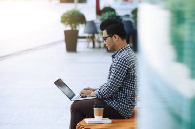 Yazılım mühendisi modern ofiste tezgah üzerinde oturan ve dizüstü bilgisayar üzerinde çalışıyor