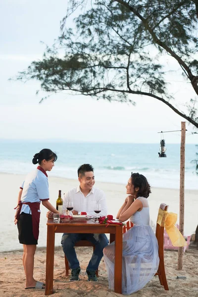 年轻的亚洲夫妇与女服务员交谈 并在海滩上的浪漫晚餐点食物 — 图库照片