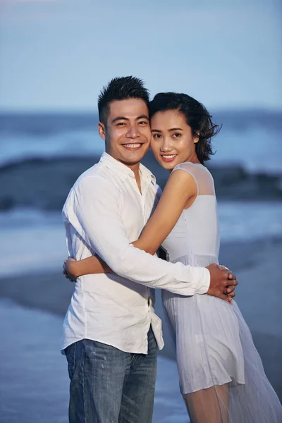 Happy Knuffelen Jong Paar Staande Het Strand Glimlachen Bij Camera — Stockfoto