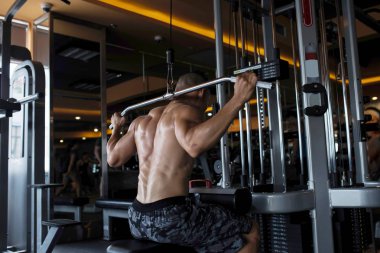 Spor salonunda makine aşağı çekin üzerinde güçlü vücut geliştirmeci egzersiz