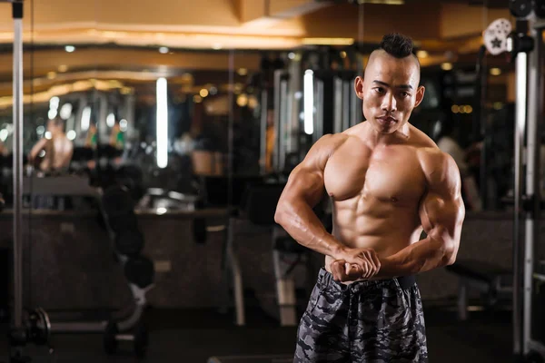 严肃英俊的年轻亚洲男人与泵送胸部和手臂站在健身房 — 图库照片