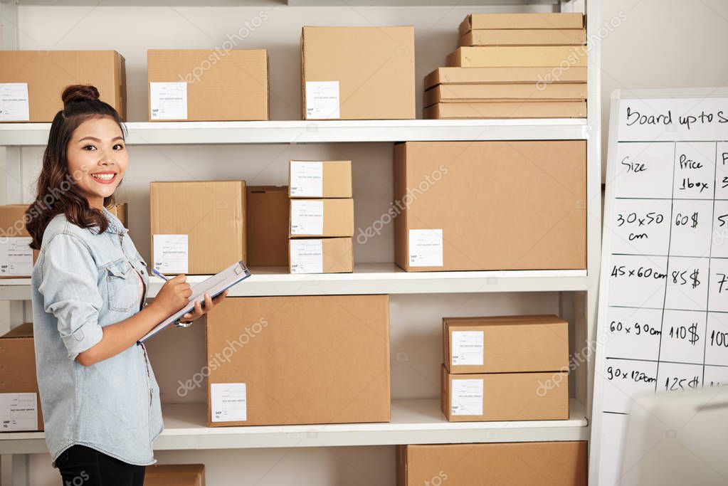 Portrait of female office worker standing near the shelves with online shopping box parcel in warehouse