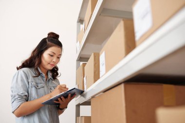 Parsel ile rafların yanında ayakta iken notları yapma Asya kadın