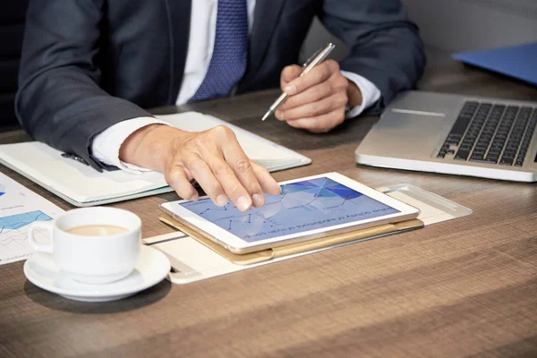 Faceless shot of anonymous formal man sitting at table in office with papers and using tablet