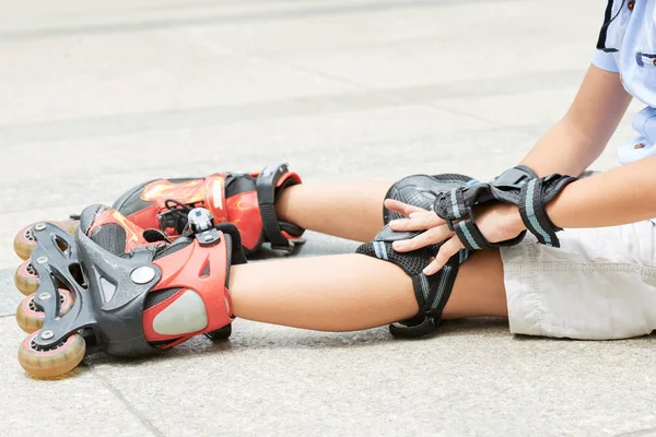 彼女の膝の痛みで地面に座っているローラースケートの女の子 — ストック写真