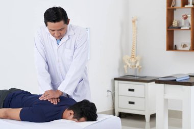 Profesyonel Vietnamlı chiropractor erkek hastanın omurgasını ayarlamak için hareket itme yapıyor