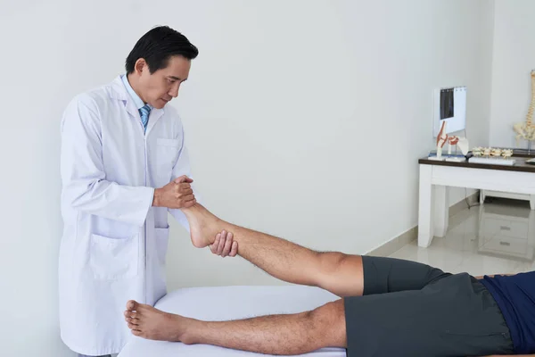 Fizjoterapeuta Ciągnący Nogę Młodego Pacjenta Podczas Sesji Terapeutyczny — Zdjęcie stockowe
