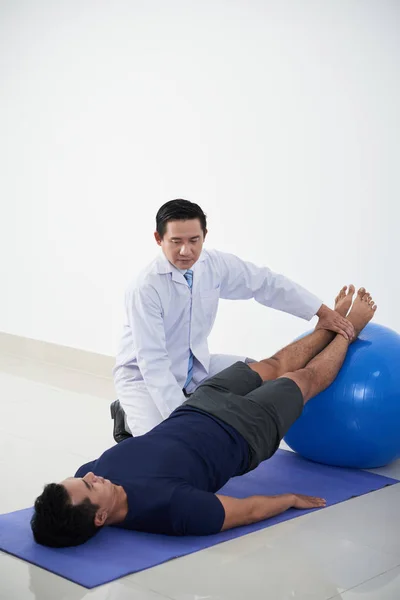 物理治疗师在康复治疗过程中将病人的腿放在适合的球上 — 图库照片