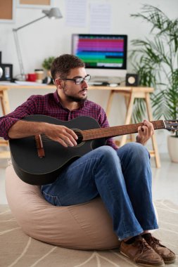 Gözlüklü genç adam kanepede oturan ve gitar oynuyor 