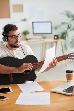 Gözlüklü genç adam gitar ve çarşaf müzik ile masada oturan ve bir şarkı yazma