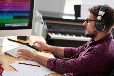 Masada oturan ve bilgisayar klavyesi yazarak kulaklık ve gözlük genç besteci, o yeni bir şarkı kayıt