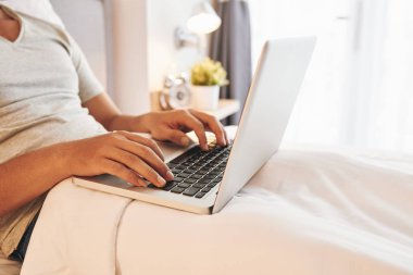 Yatakta oturan ve laptop üzerinde çalışan genç adam kırpılmış görüntü