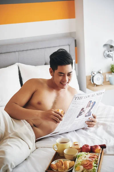 Glimlachende Jonge Man Eten Ontbijt Lezen Krant Bed — Stockfoto