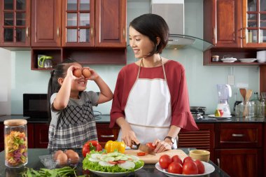 Gülümseyen genç kadın yemek pişirirken yumurtaile oynarken küçük kızına bakıyor