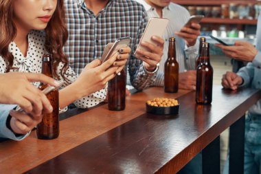 Sosyal medya ile ayrı bira şişeleri ile masada oturan ve akıllı telefonlar kullanarak arkadaşlar yüzsüz çekim