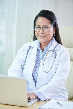 Neşeli Tay kadın doktor onun ofis masasında bilgisayar üzerinde çalışıyor