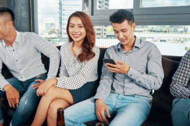 Güzel Asyalı kadın kanepede erkeklerle oturan ve partide toplarken birlikte rahatlatıcı 