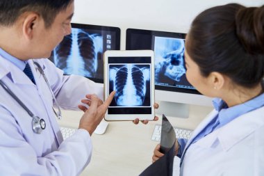 Olgun erkek radyolog akciğerlerin x-ray görüntü ile tablet pc tutan ve hastanede asistanı ile sorunu tartışıyor