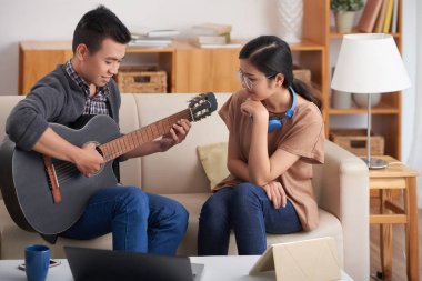 Güzel gülümseyen genç kadın nasıl erkek arkadaşı gitar çalarken bakıyor