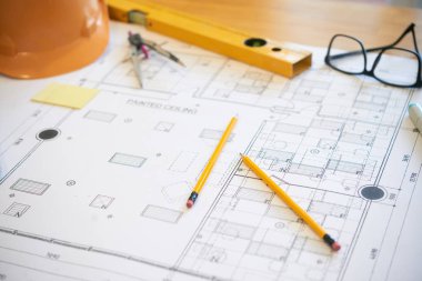Ofis masasında gözlük ve hardhat yakınında inşaat planı üzerinde yatan iki kalem