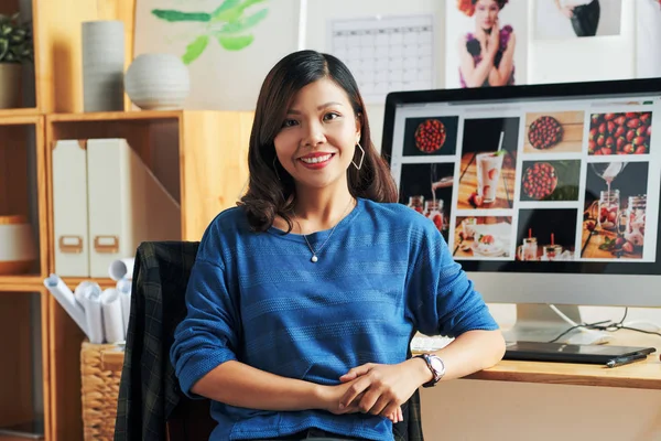 Portrait of smiling Vietnamese graphic designer at her table in office