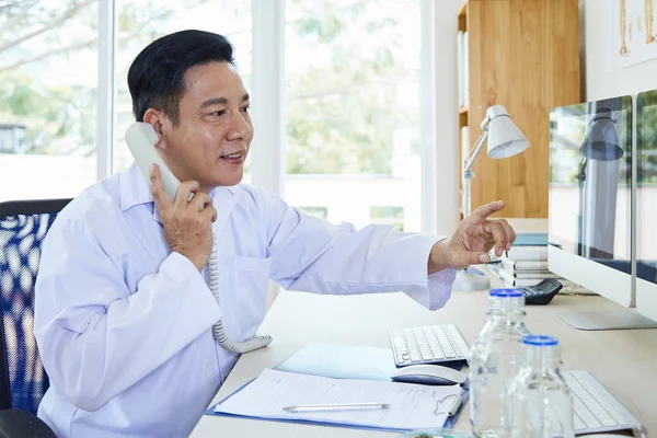 Mature Doctor Wearing White Medical Uniform Talking Phone Pointing Computer — Stock Photo, Image