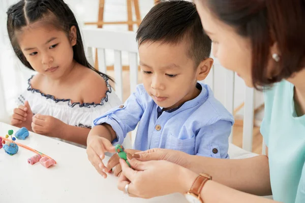 美術のクラスでかわいいアジアの男の子と女の子にプラスチックを表示し 助ける教師の女性 — ストック写真