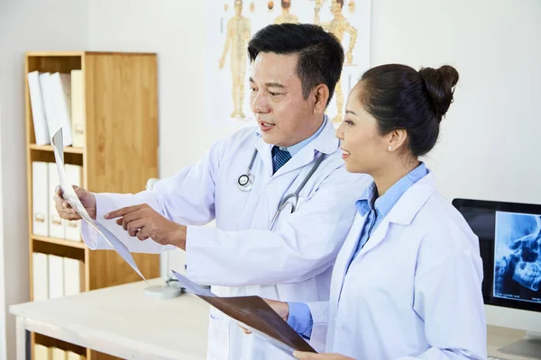两名亚洲医学专家统一站立 指着X光图像 在办公室一起讨论 — 图库照片