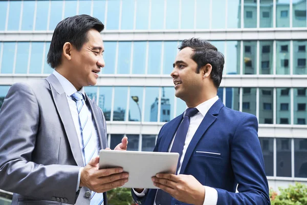 2人のビジネス仲間が屋外に立ち 現代のオフィスビルを背景にデジタルタブレットでプレゼンテーションを議論 — ストック写真
