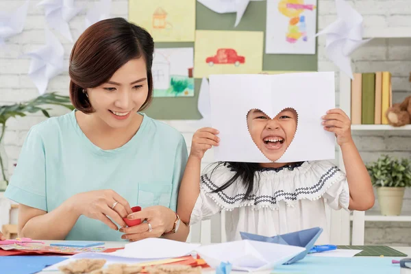 小亚洲女孩坐在老师和乐趣与剪纸在艺术课上切出心 — 图库照片