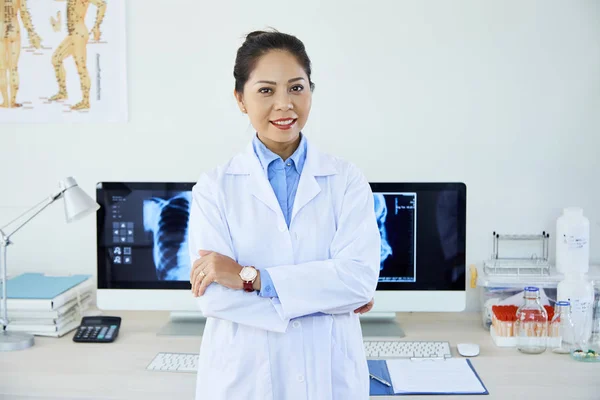 Portrait of young Asian radiologist standing in lab coat with arms crossed and smiling while working with x-ray images