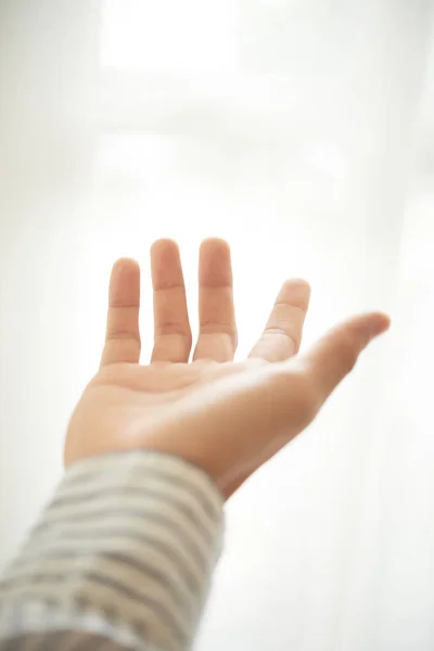 Crop hand of unrecognizable person reaching out and offering help on white background in light room