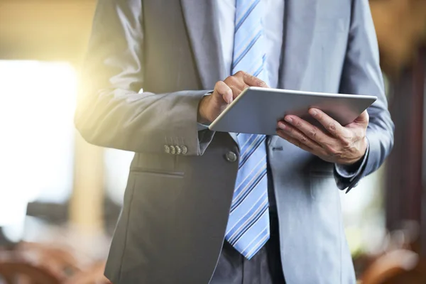 Close-up of male executive in suit standing and holding digital tablet, he typing a message or working online