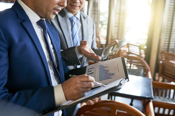 Financial adviser analyzing financial report together with his colleague who using tablet pc while they standing in cafe