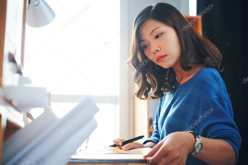 Serious pensive young woman checking documents on her table