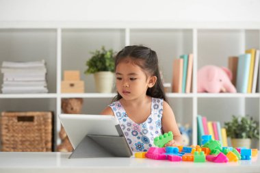 Küçük kız bloklardan bir kule bina ve masada dijital tablet kullanarak