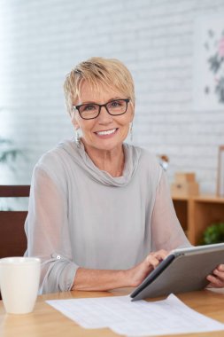 Masasında tablet bilgisayar üzerinde çalışan zarif üst düzey iş kadını