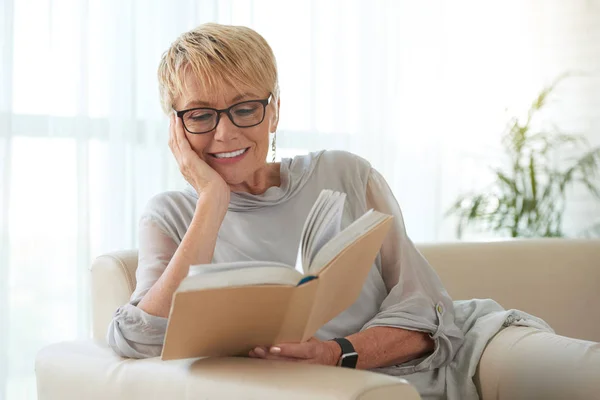 Starší Blondýnka Brýlích Odpočívajícím Pohovce Čte Knihu — Stock fotografie