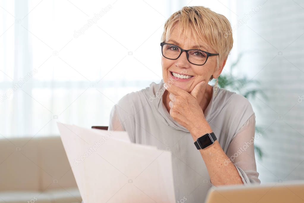 Portrait of smiling senior woman with documents looking at camera