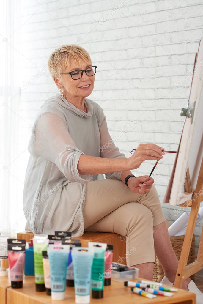 Smiling elderly woman painting on canvas in art studio