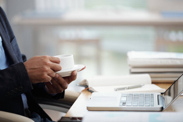 Cropped image of businessman drinking coffee and reading news or e-mails on laptop screen