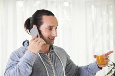 Korkmuş duygusal genç adam telefonda konuşurken ve elinde meyve suyu cam bakarak