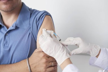 Erkek hastaya aşı enjeksiyonu yapan şırıngalı doktorun elleri