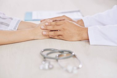 Muayeneden ve muayeneden sonra hasta ile el ele tutuşan genç bir doktor.