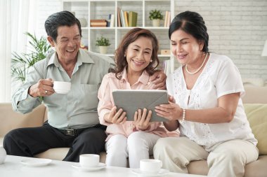 Mutlu yaşlı insanlar çay içme ve evde tablet bilgisayarda fotoğrafları bakarak