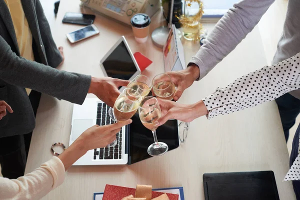 Group of colleagues toasting with champagne glasses over office table to celebrate Christmas